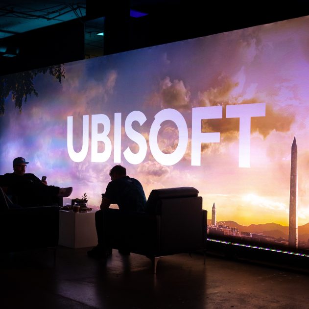 Los Angeles, Californie - 12 juin 2023 : Deux personnes s'attardent à l'événement du jeu vidéo Ubisoft Forward, avec un grand panneau d'affichage de Assassin's Creed : Mirage.