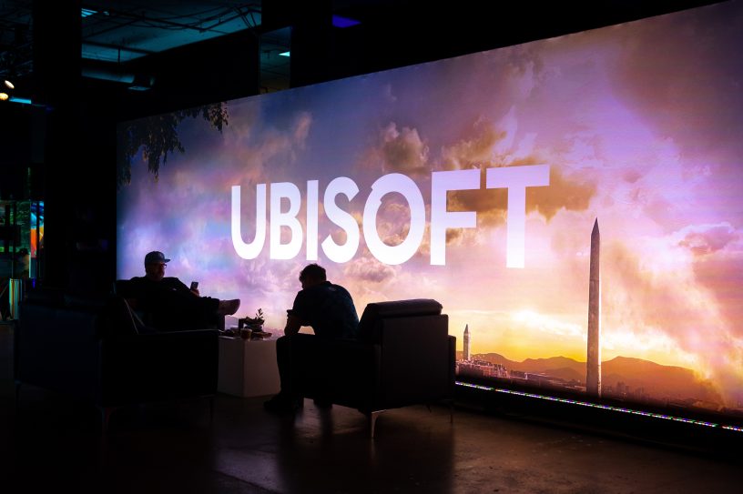 Los Angeles, Californie - 12 juin 2023 : Deux personnes s'attardent à l'événement du jeu vidéo Ubisoft Forward, avec un grand panneau d'affichage de Assassin's Creed : Mirage.